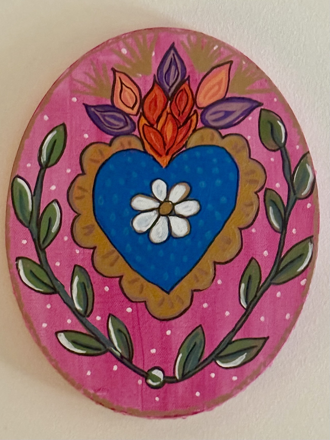 Oval folk-art painting of a blue heart and white flower framed by pink petals