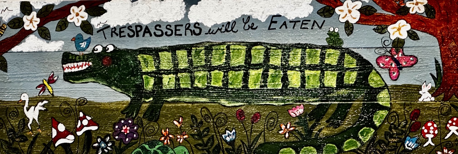 Green alligator among magnolia blossoms and flowers beneath a playful warning